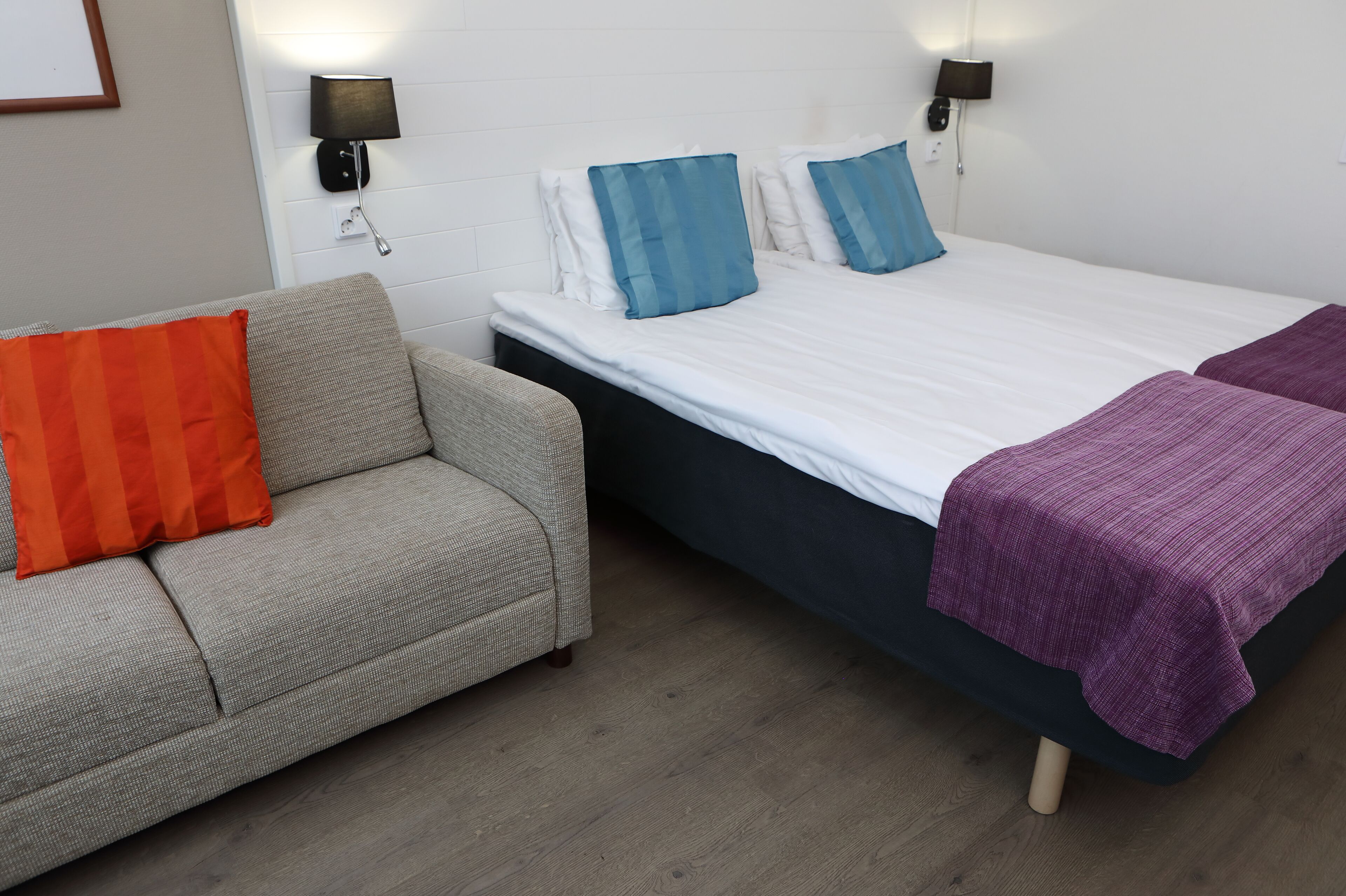A bedroom with a bed, a sofa, and two wall-mounted lamps.