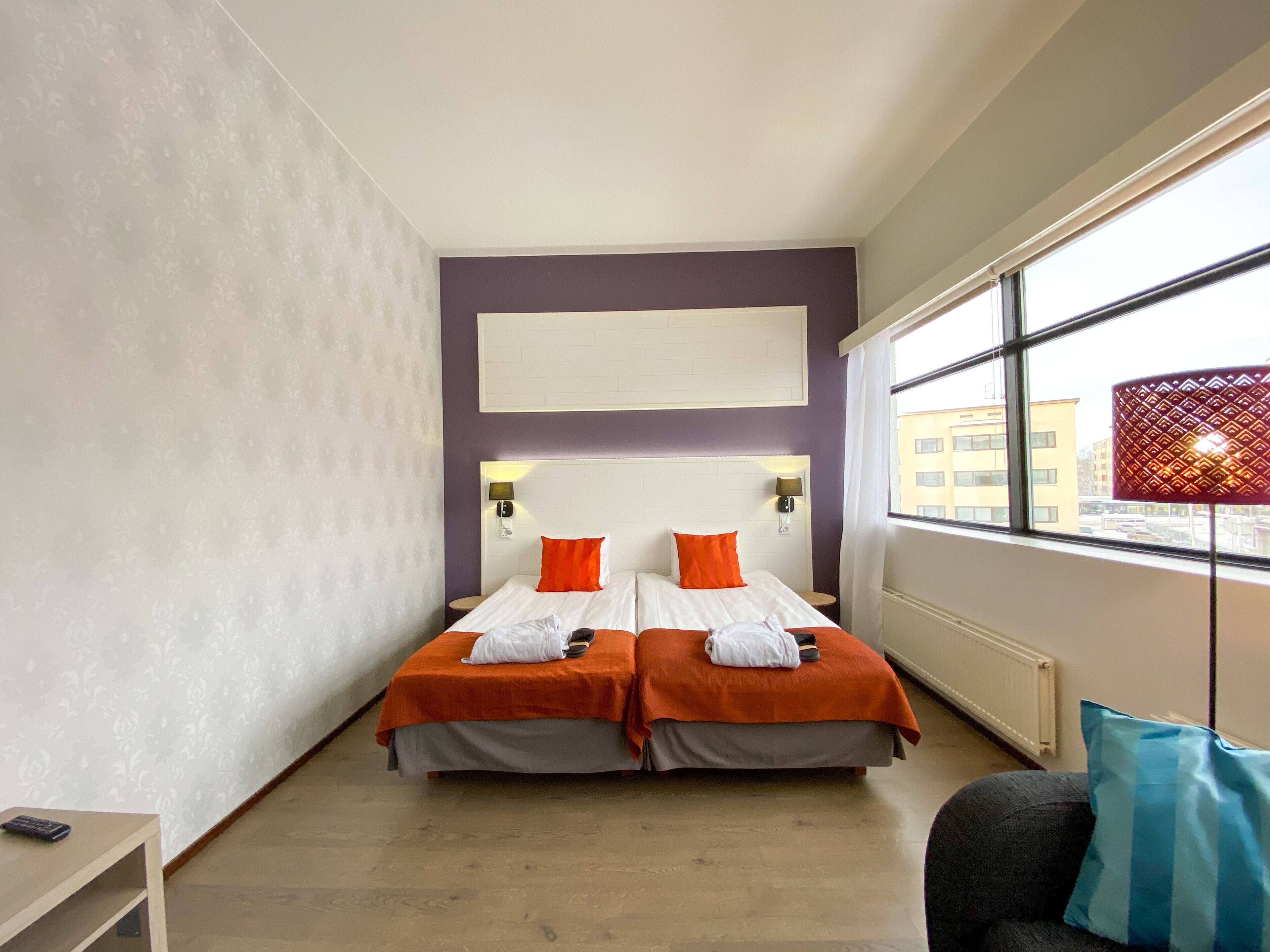 Habitación de hotel con dos camas, un ventanal grande y vistas a edificios.