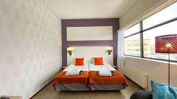 Habitación de hotel con dos camas, un ventanal grande y vistas a edificios.