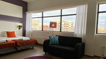 A modern living room with a sofa, a round purple rug, and a window with curtains.