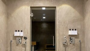 A modern bathroom with two showerheads, a glass-enclosed shower area, and a wooden staircase leading to a dark room. - Hotel Fabrik Forssa (Forssa)