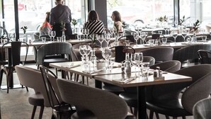 A restaurant with multiple tables set for dining, large windows, and a view of the street outside. - Hotel Fabrik Forssa (Forssa)