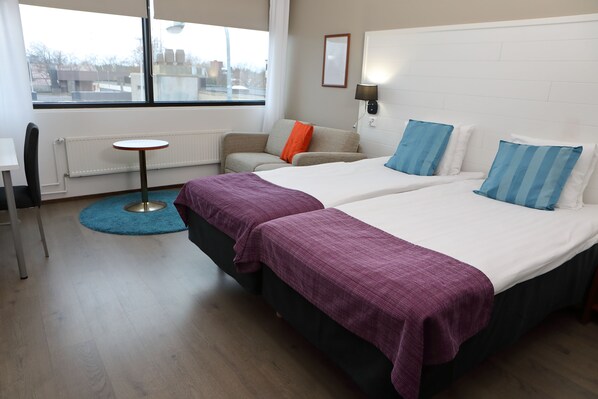 A hotel room with two beds, a small table, a chair, and a view of the outside. - Hotel Fabrik Forssa (Forssa)