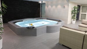 A modern indoor pool area with a hot tub, seating, and potted plants. - Hotel Fabrik Forssa (Forssa)