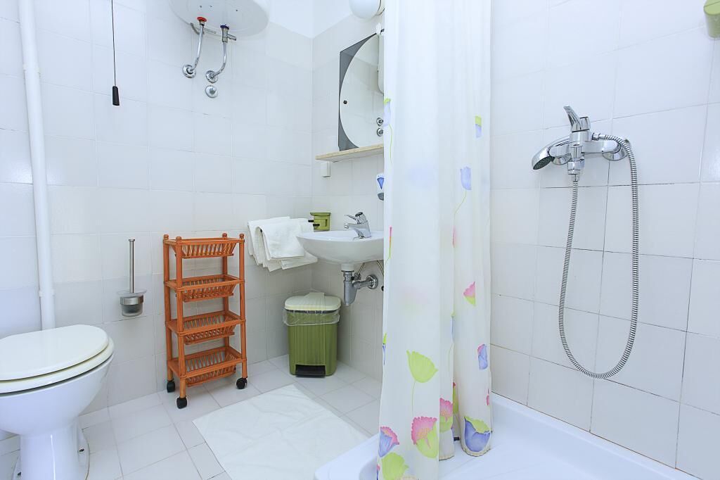 A bathroom with a toilet, sink, shower, and a shelf with towels.