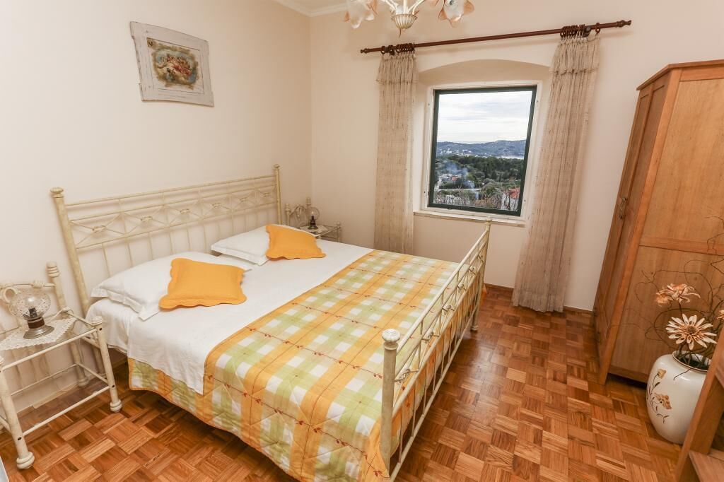 A bedroom with a bed, a nightstand, a window with a view, and a wooden wardrobe.