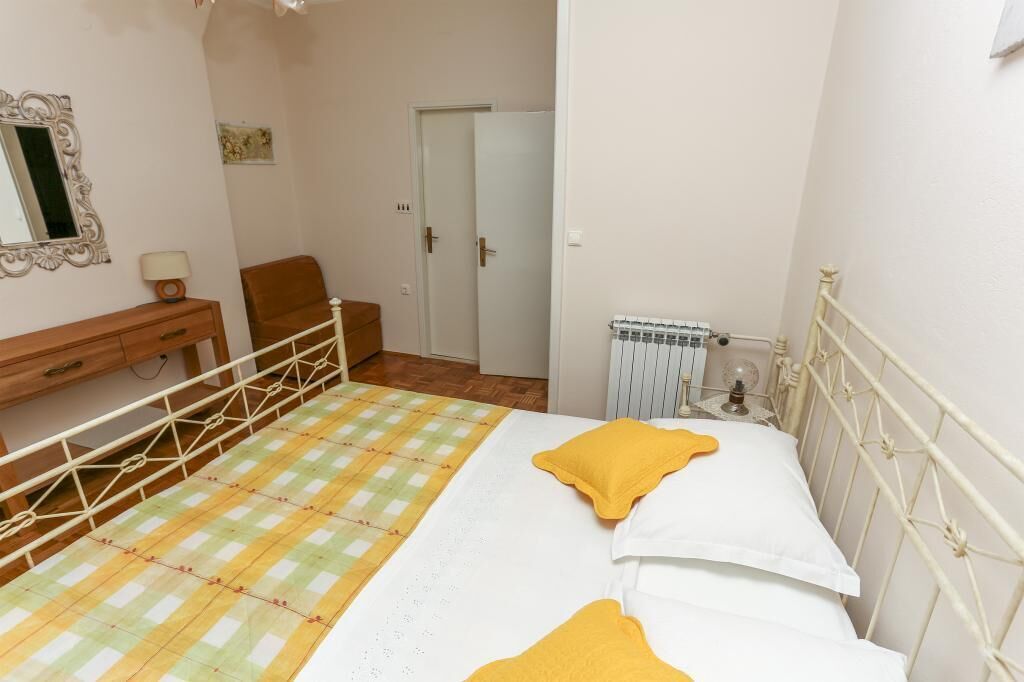A bedroom with a bed, a chair, a dresser, a mirror, and a radiator.