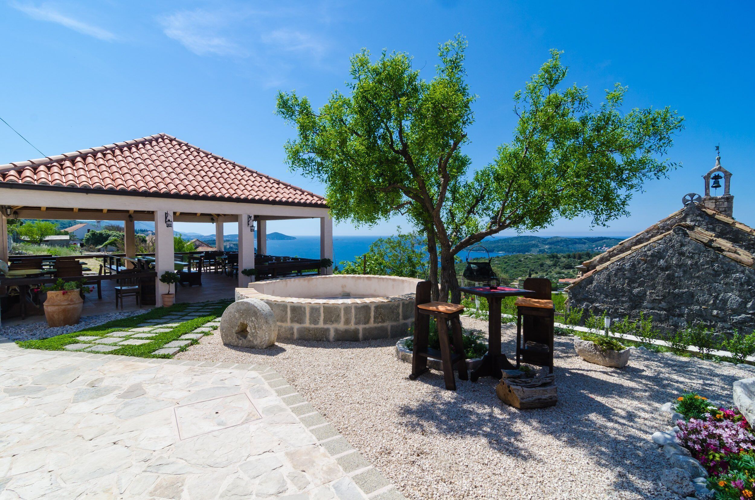 A covered outdoor seating area with stone flooring, a fire pit, and a view of the sea.