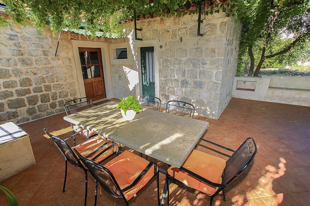 Un patio al aire libre con paredes de piedra, una mesa, sillas, una planta en maceta y una puerta.