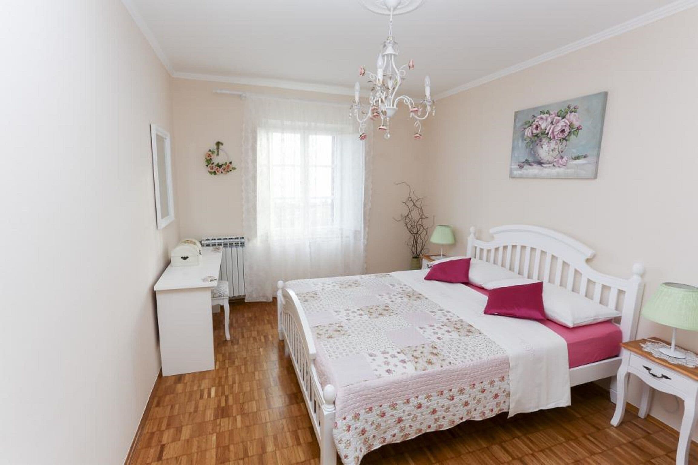 Une chambre à coucher avec un lit blanc, un bureau, une chaise, une lampe et un tableau accroché au mur.