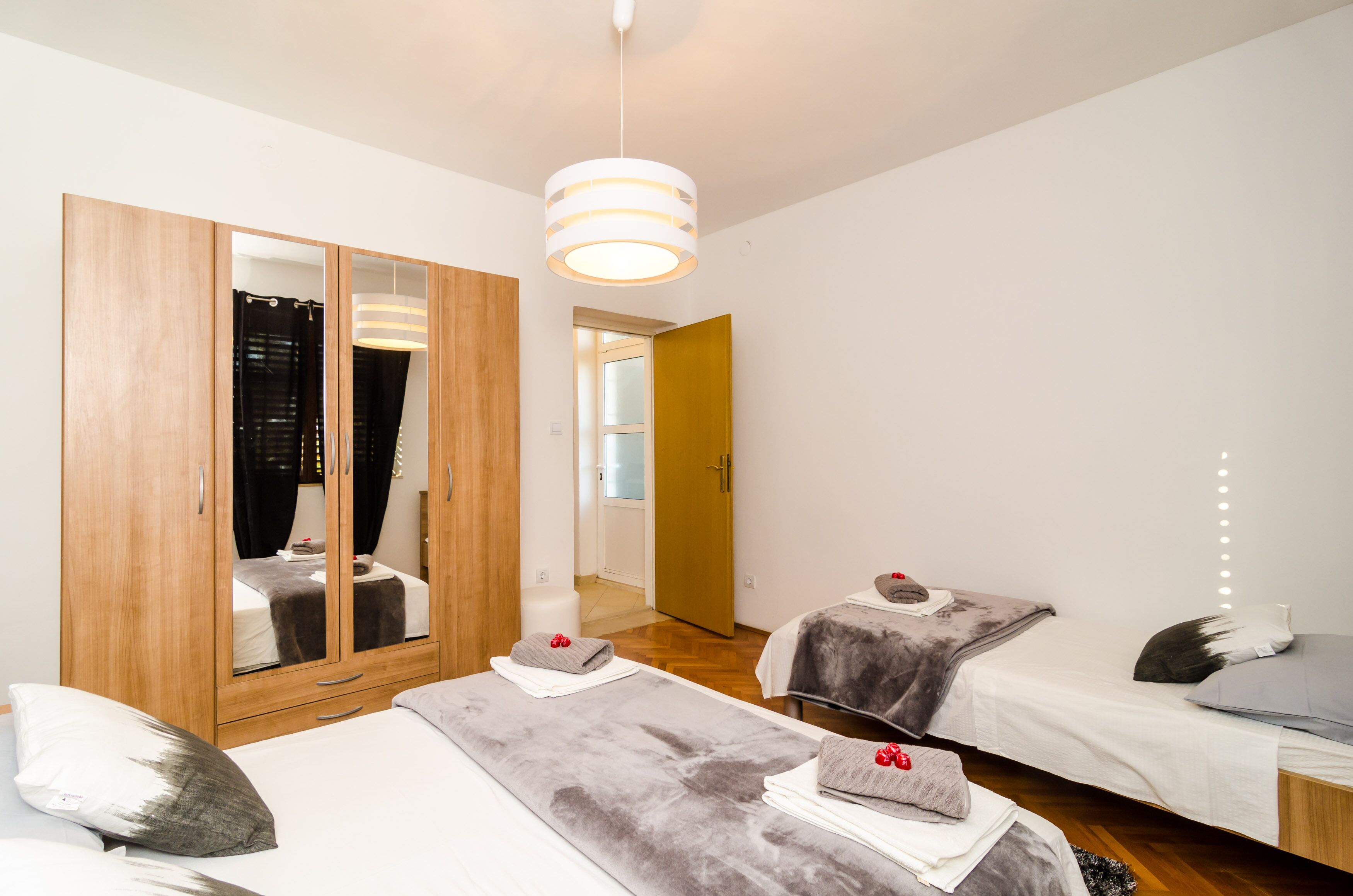 A modern bedroom with a large wardrobe, two beds, a mirror, and a hanging light fixture.