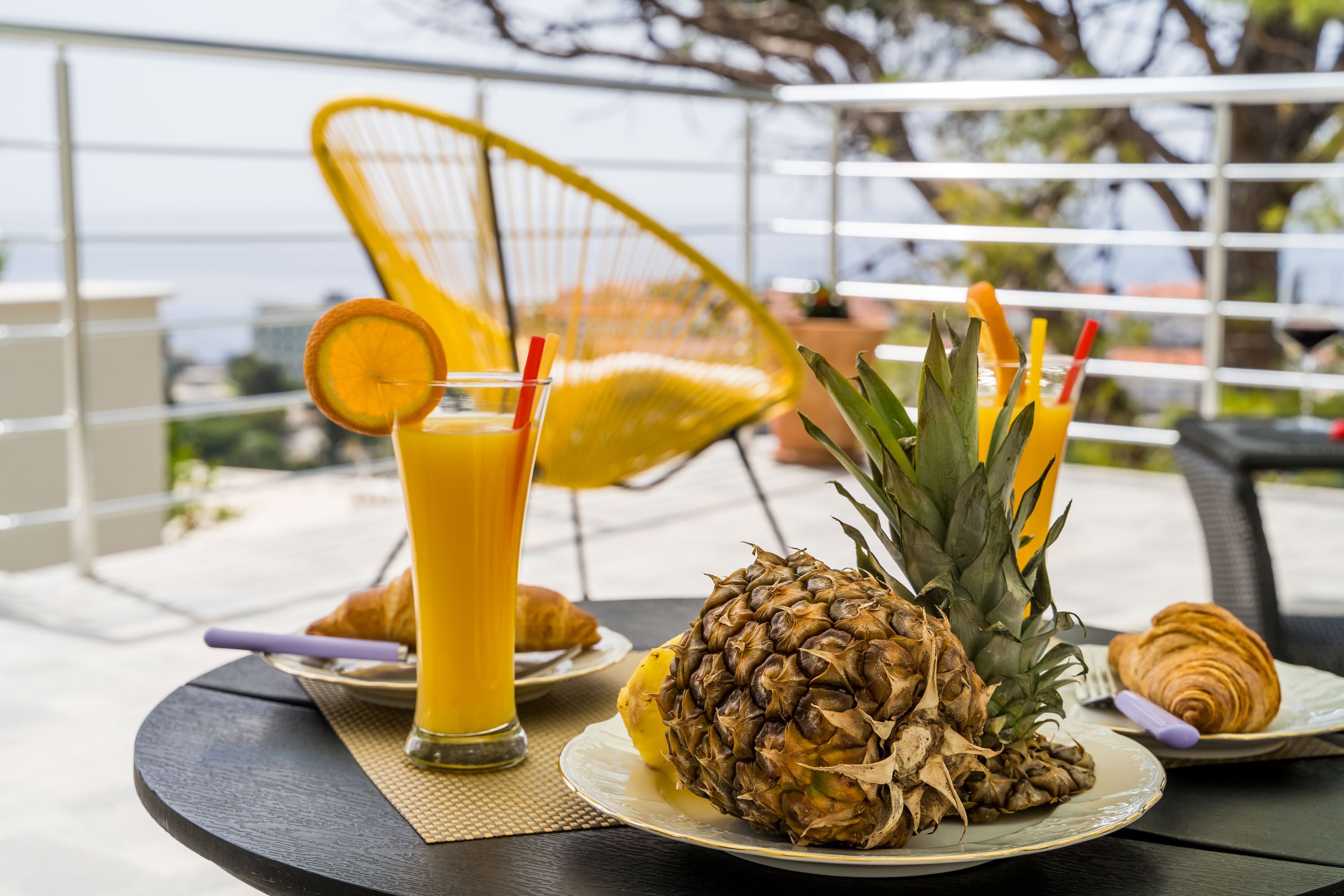 A tropical breakfast setting with a pineapple, croissant, and orange juice on a table.