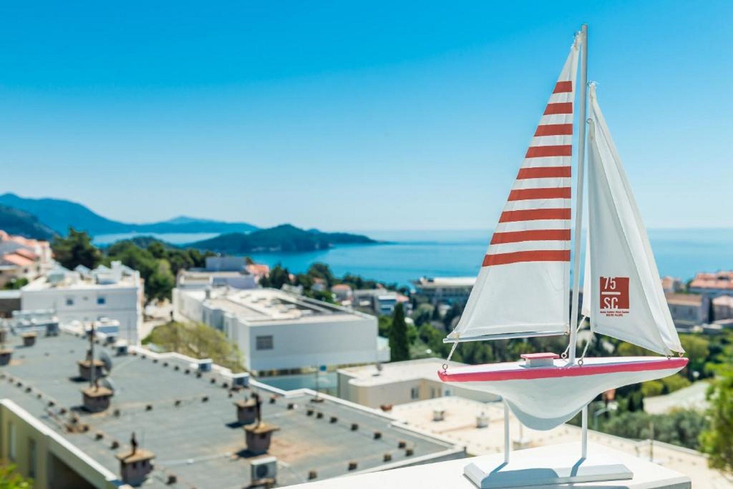 A sailboat model on a rooftop with a cityscape and mountains in the background.