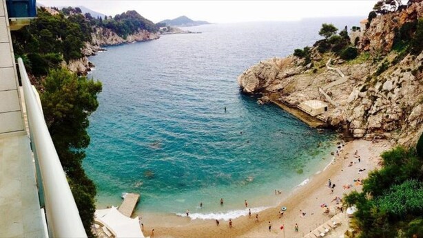 A coastal beach with rocky cliffs, clear blue water, and a sandy shore. - Apartment Eulalija (Dubrovnik)