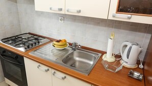 A kitchen with a gas stove, sink, and a bowl of fruit on the counter. - Apartments Depozit-joky (Dubrovnik)