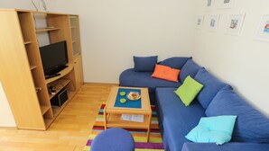 A living room with a TV, sofa, and a small table with a plate of food. - Apartments Depozit-joky (Dubrovnik)