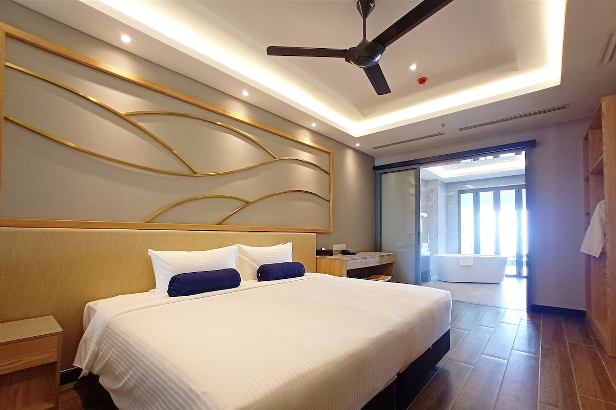 A modern hotel room with a large bed, a ceiling fan, and a view of the bathroom.