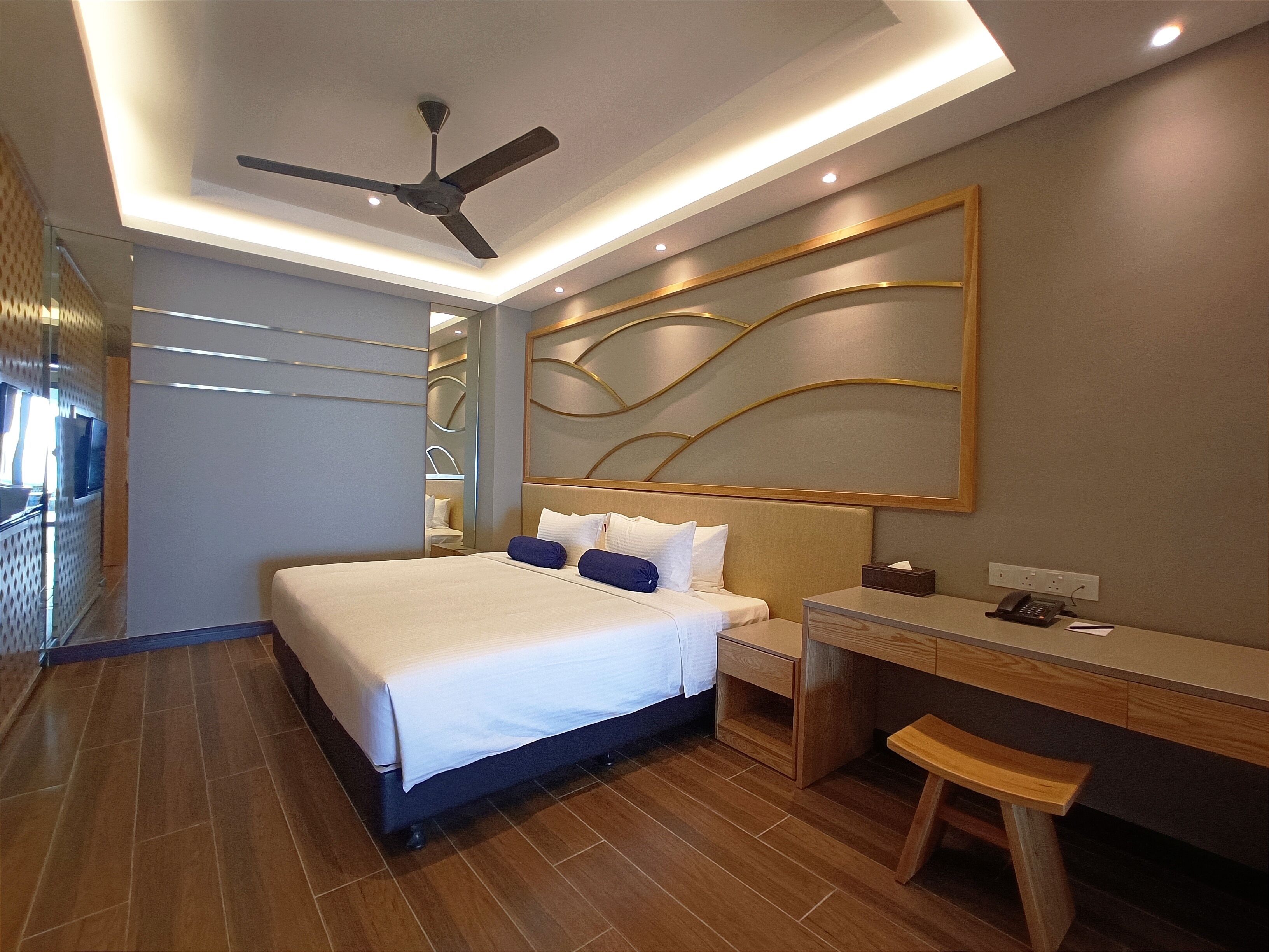 A modern hotel room with a bed, desk, chair, and ceiling fan.