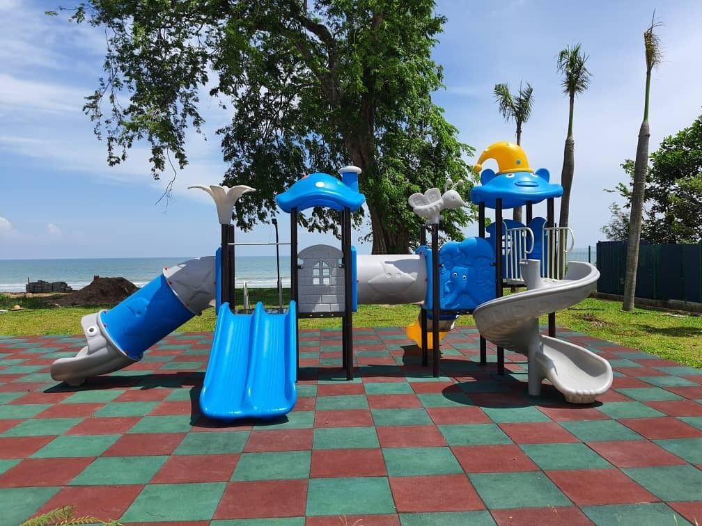 Un parque infantil con toboganes y estructuras para escalar, sobre un suelo a cuadros con vista al océano.