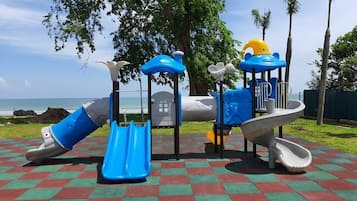 Un parque infantil con toboganes y estructuras para escalar, sobre un suelo a cuadros con vista al océano.