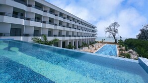 Ein modernes Hotel mit großzügiger Poolanlage, Meerblick und einem mehrstöckigen Gebäude mit Balkonen.
