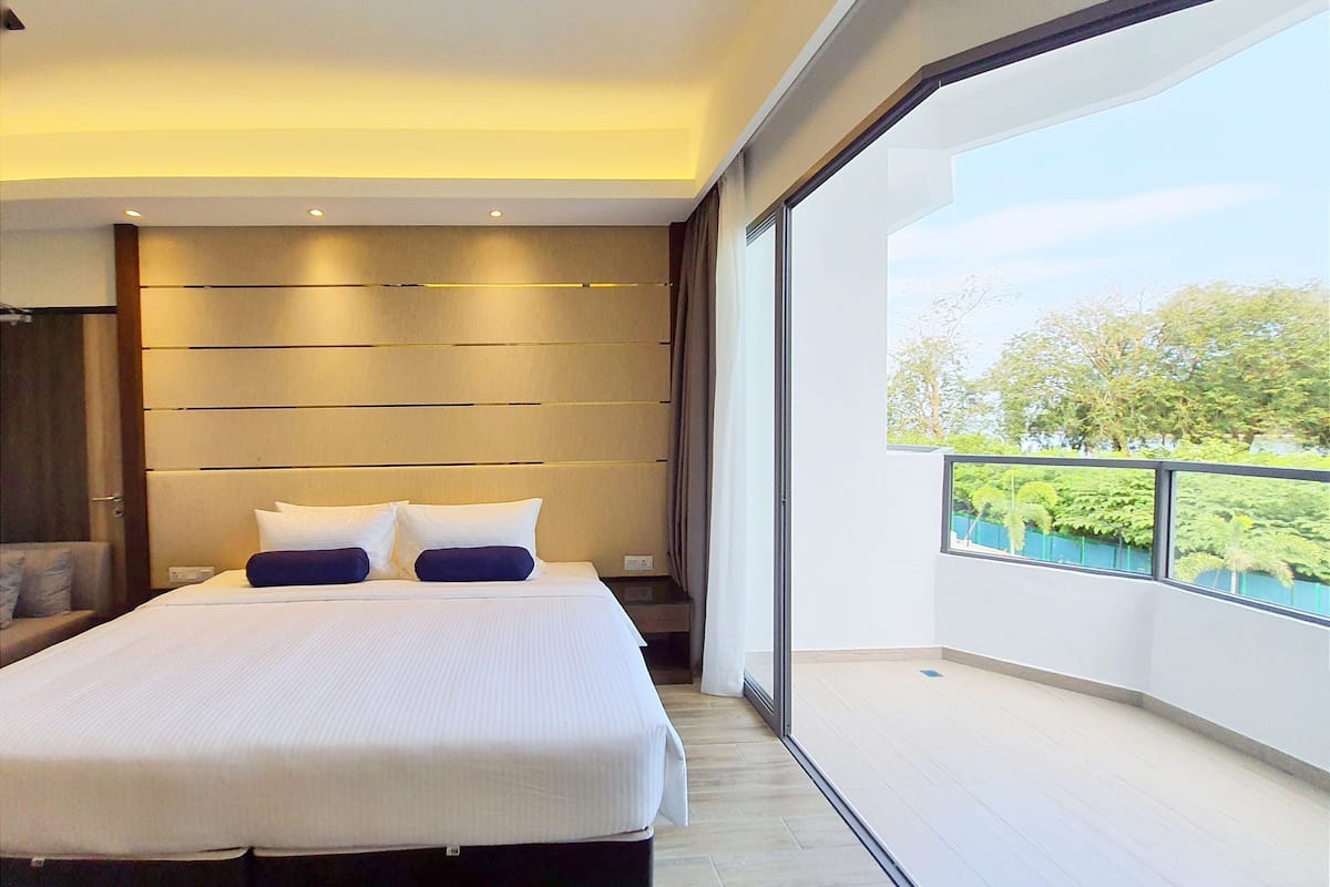 A modern bedroom with a large bed, a view of greenery through a balcony, and a contemporary design.