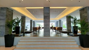 Eine moderne Lobby mit einer zentralen Treppe, großen Säulen und Sitzbereichen.
