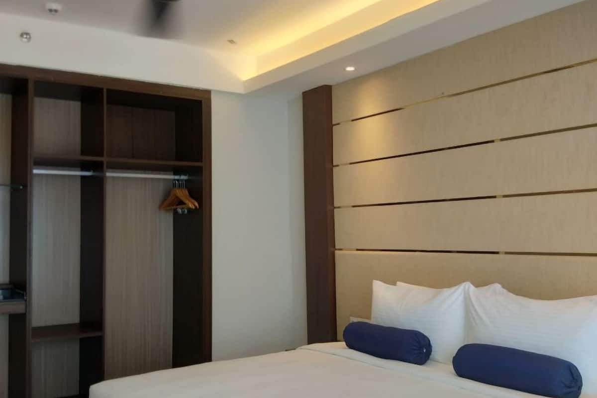A hotel room with a large bed, a ceiling fan, a wardrobe, and a headboard with horizontal lines.