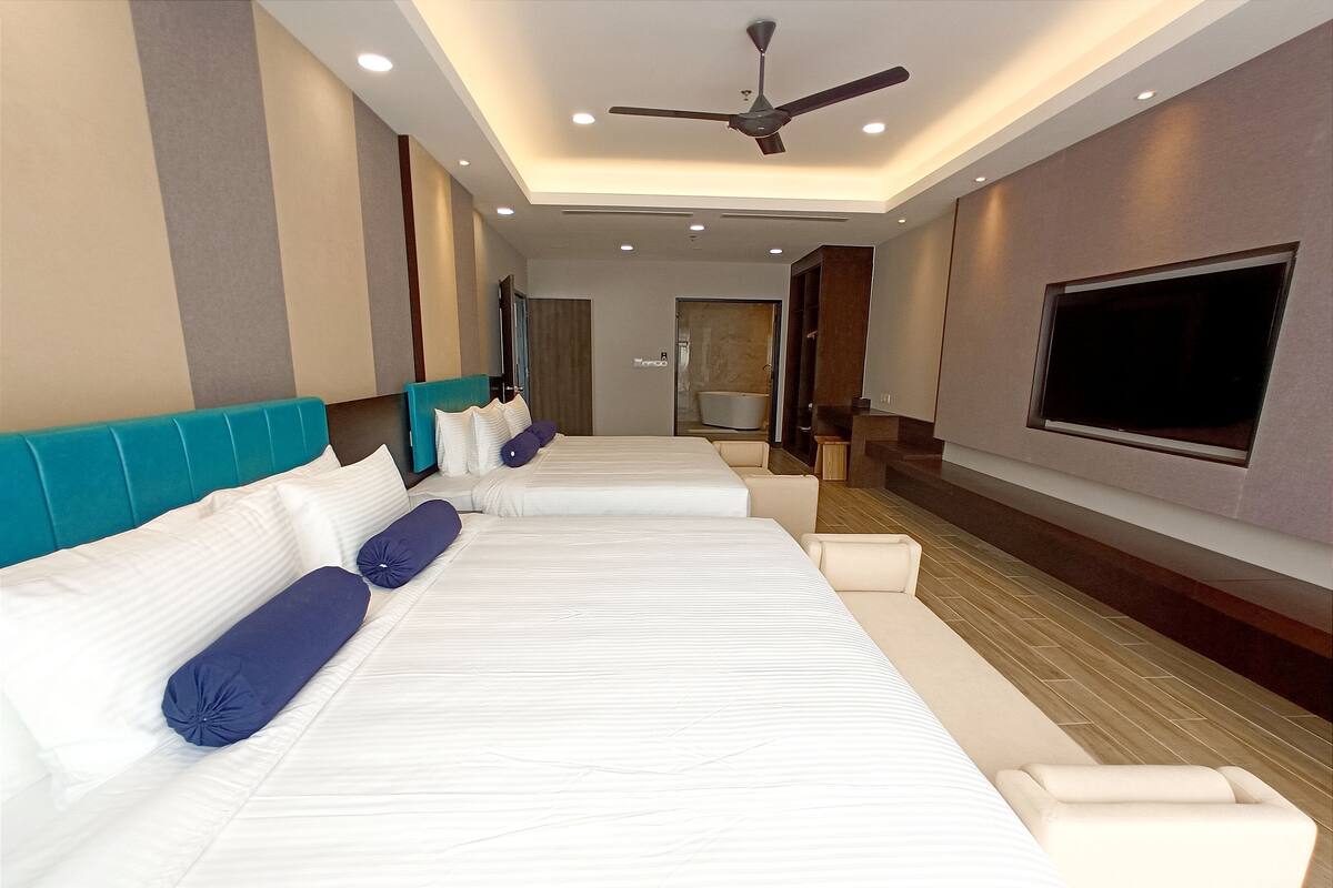 A hotel room with two beds, a ceiling fan, recessed lighting, a TV, and a bathtub.