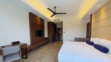 A modern hotel room with a large bed, a desk, a TV mounted on the wall, and a ceiling fan.