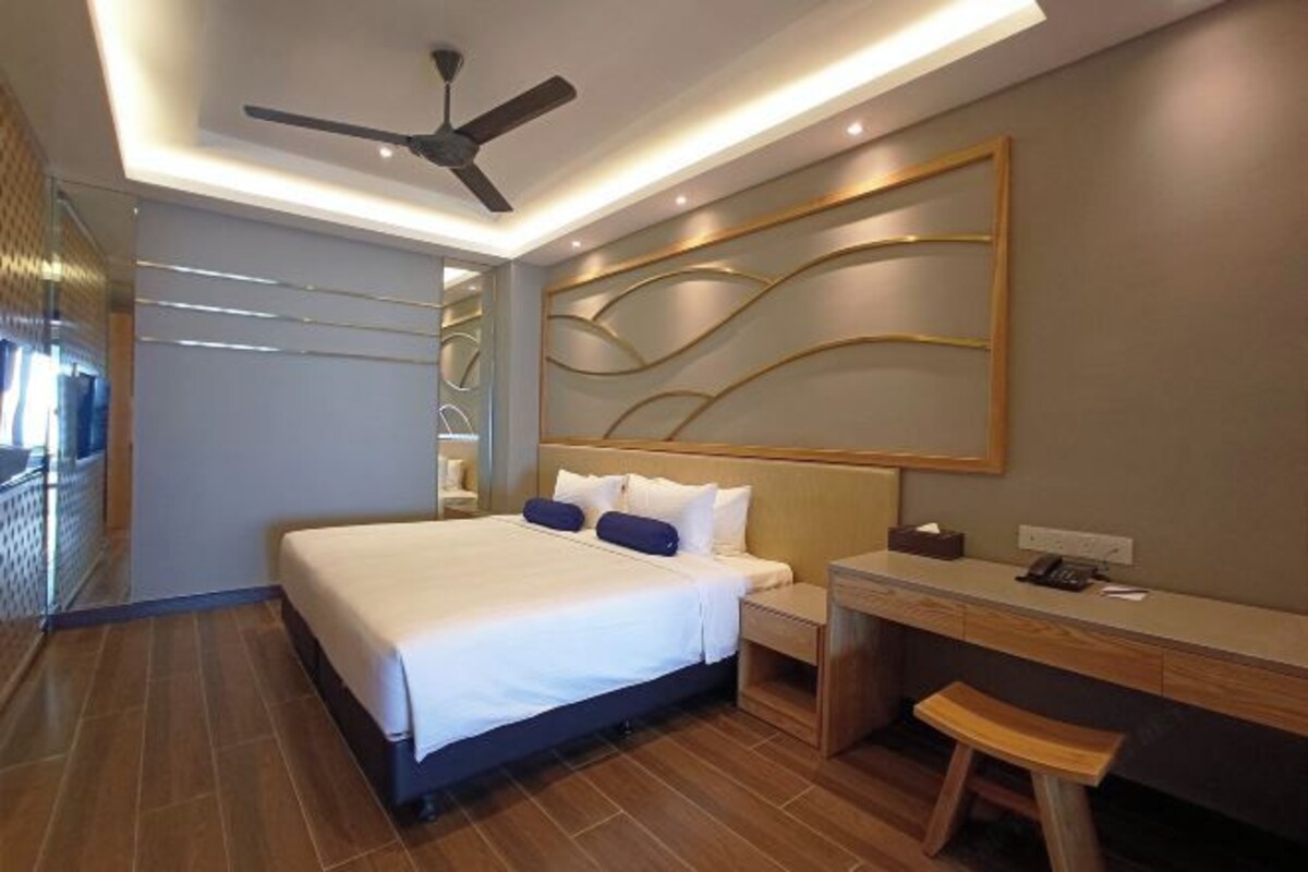 A modern hotel room with a large bed, a desk, and a ceiling fan.