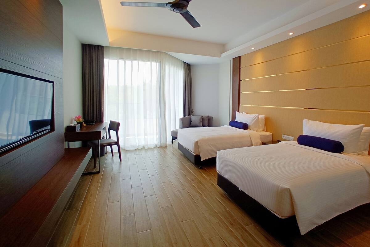 A hotel room with two beds, a desk, a TV, and a ceiling fan.