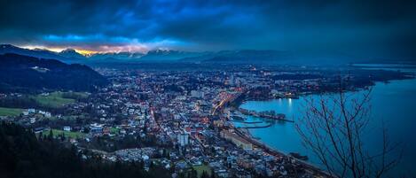 Vista panorâmica de uma cidade com um rio, montanhas ao fundo e uma ponte ligando duas partes da cidade.