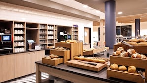 A bakery counter with bread and pastries, a coffee machine, and shelves with cups and glasses.