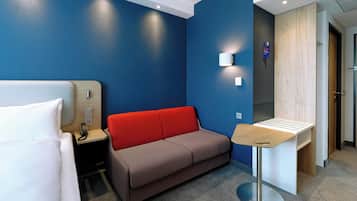 Ein Hotelzimmer mit einem Bett, einer rotbraunen Couch, einem kleinen Tisch und einer Wandleuchte.