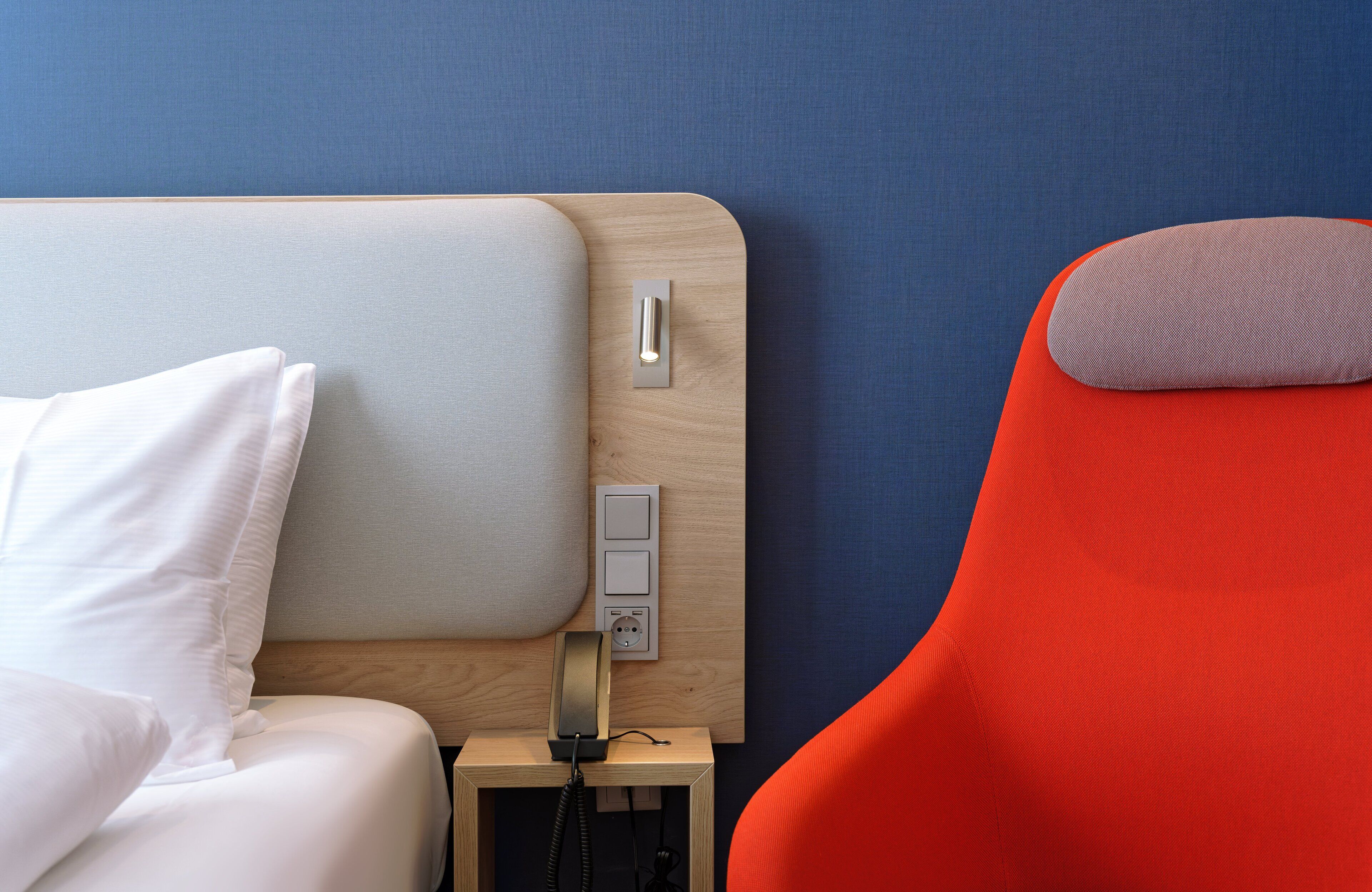 Ein Bett mit weißer Bettwäsche und ein Nachttisch mit Telefon und Steckdose.
