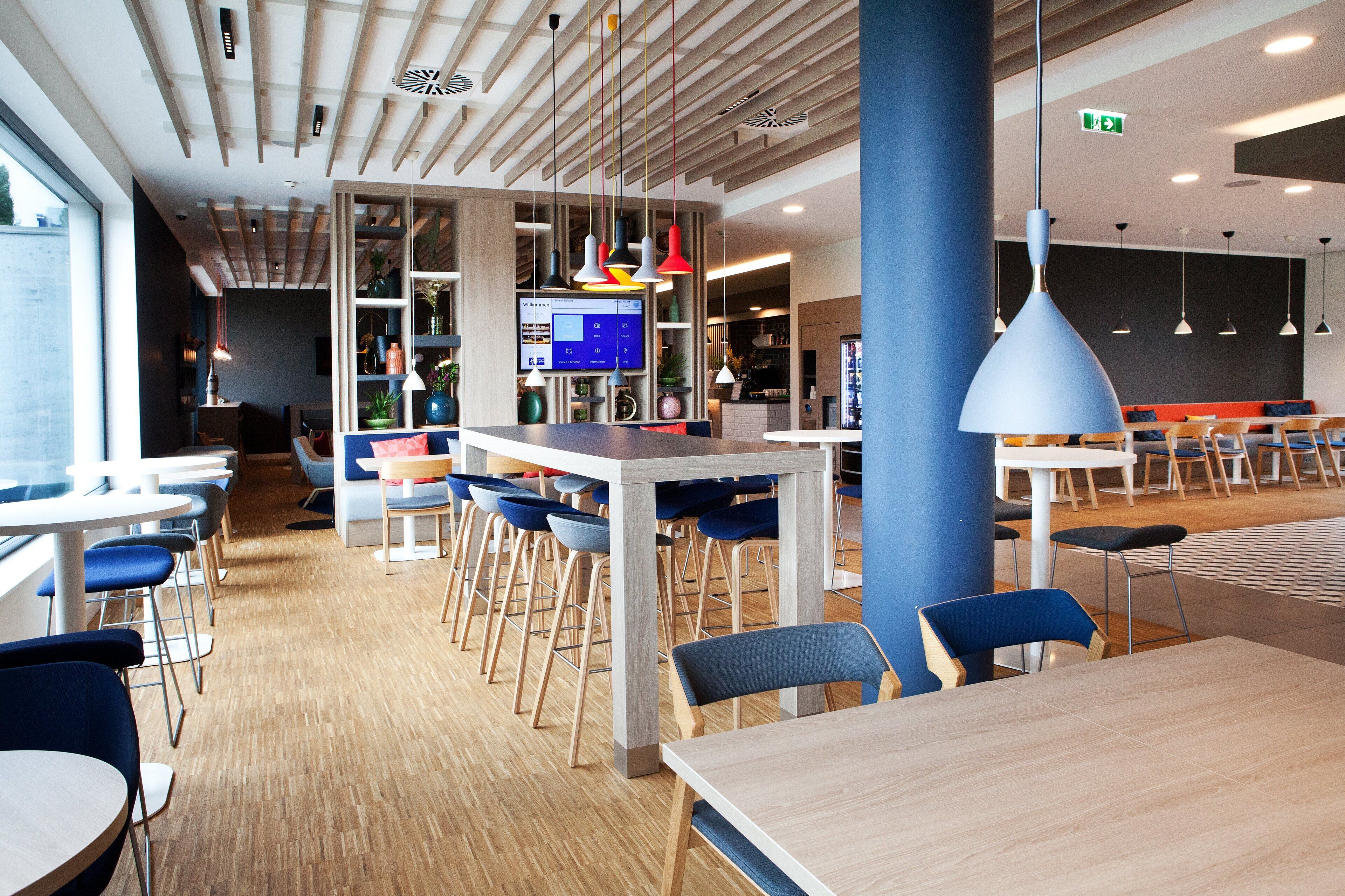 A modern cafeteria with wooden flooring, blue and white tables, and chairs.