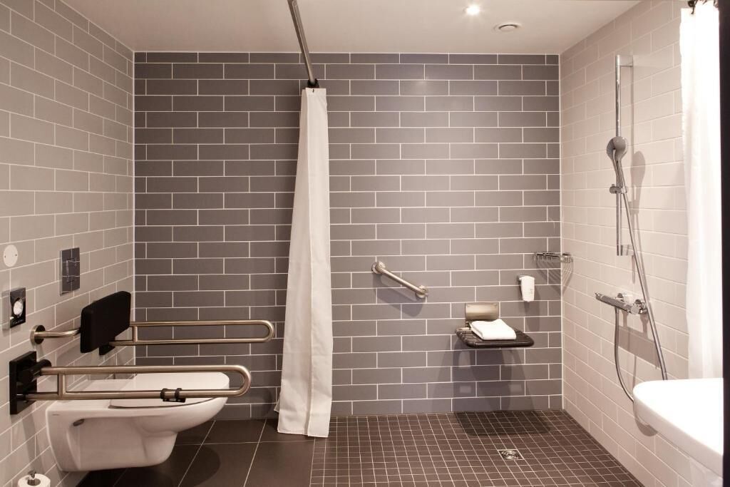Une salle de bain moderne équipée de toilettes, d’une douche et de barres d’appui.
