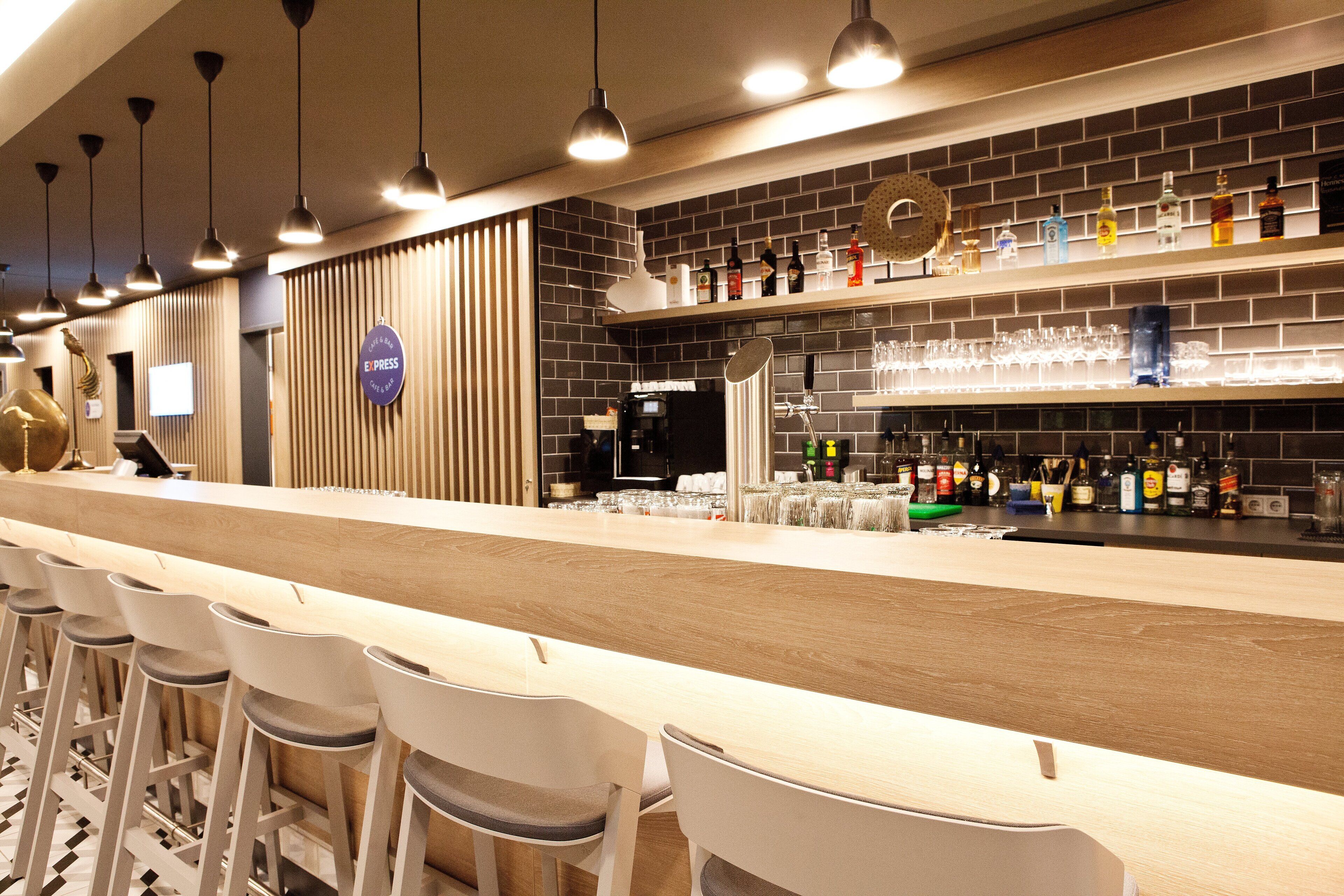 Angolo bar con un lungo bancone, diversi sgabelli e un'ampia scelta di bottiglie e bicchieri sugli scaffali.