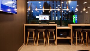 A modern bar area with wooden stools and a digital screen displaying information.