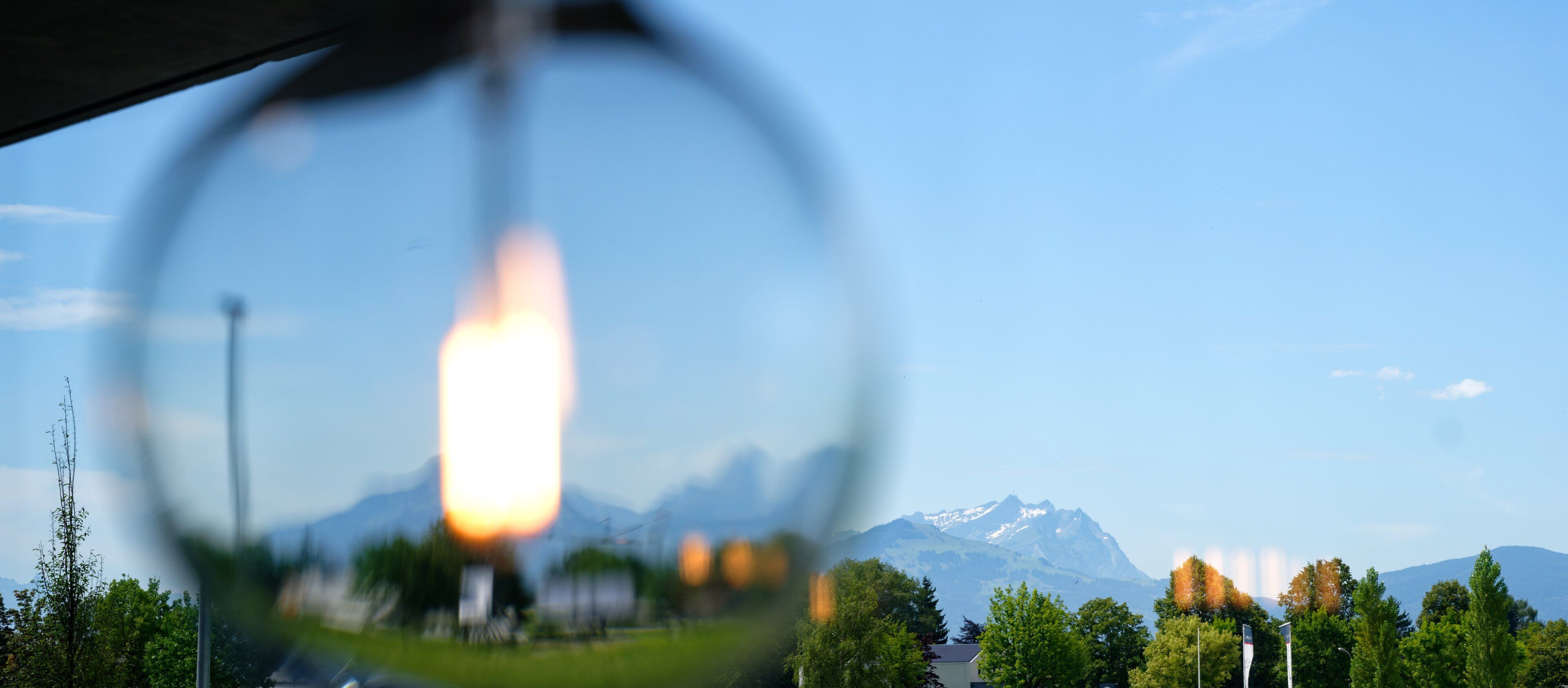 A view through a window with a clear sky, mountains, and trees in the background.