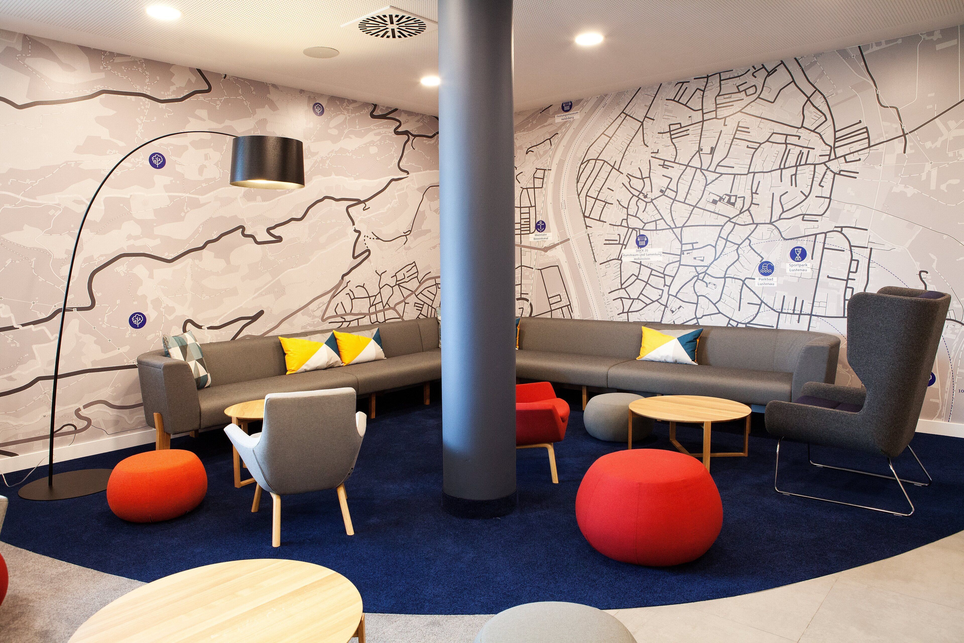A modern lounge area with sofas, chairs, and ottomans arranged around a central pillar.
