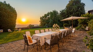 An outdoor dining area with a table set for six, surrounded by chairs, and an umbrella providing shade. - Tenuta Di Pratello 24, Emma Villas (Peccioli)