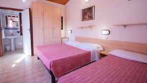 Un dormitorio con dos camas, armario de madera, mesitas de noche y un baño visible a través de una puerta abierta.