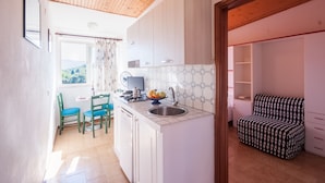 Cocina compacta con armarios blancos, un lavamanos y una zona de comedor con sillas.