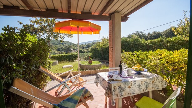 Un patio al aire libre con una mesa lista para comer, rodeado de follaje y vistas a las colinas.