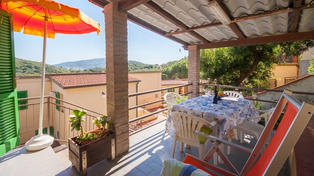 A terrace with a table set for dining, a potted plant, and an umbrella.