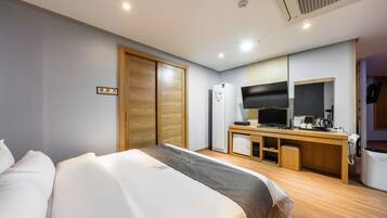 Ein Hotelzimmer mit Bett, Schreibtisch mit Computer, Kühlschrank und Fernseher.