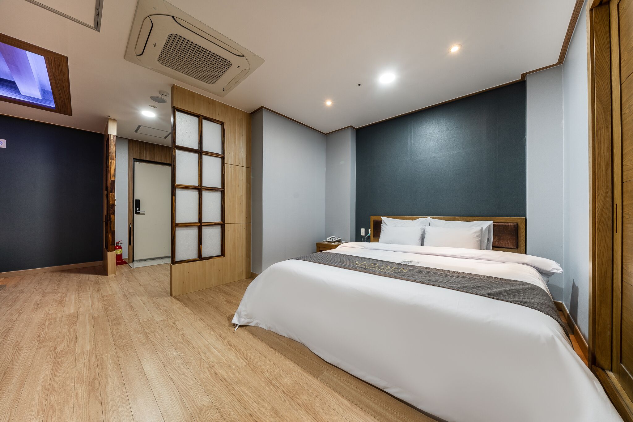 Hotellihuone, jossa on suuri sänky, puulattia, seinälle asennettu televisio ja perinteinen japanilainen liukuovi.