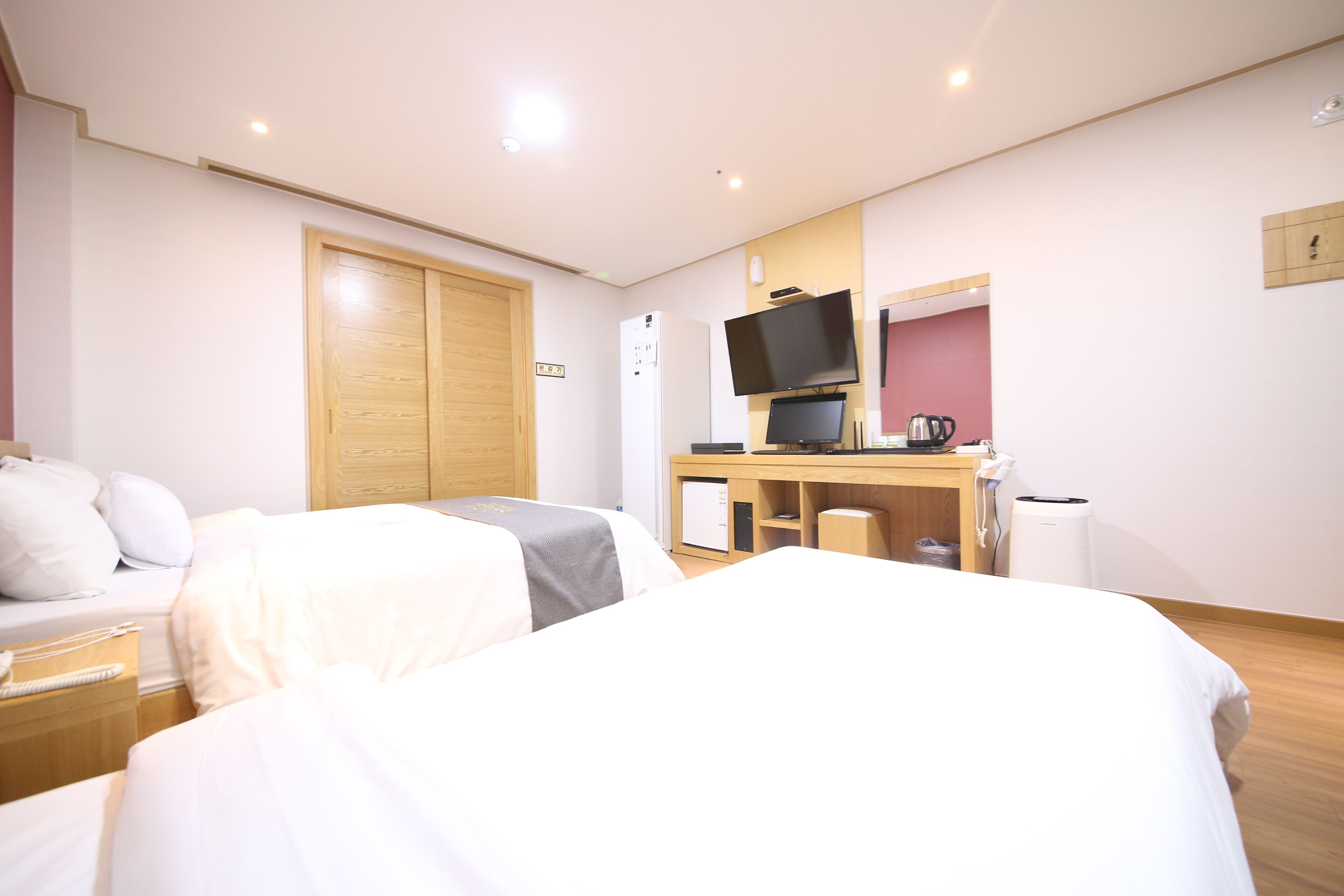 Ein Hotelzimmer mit zwei Betten, einem Schreibtisch mit Fernseher, einem Kühlschrank und einem Holzschrank.